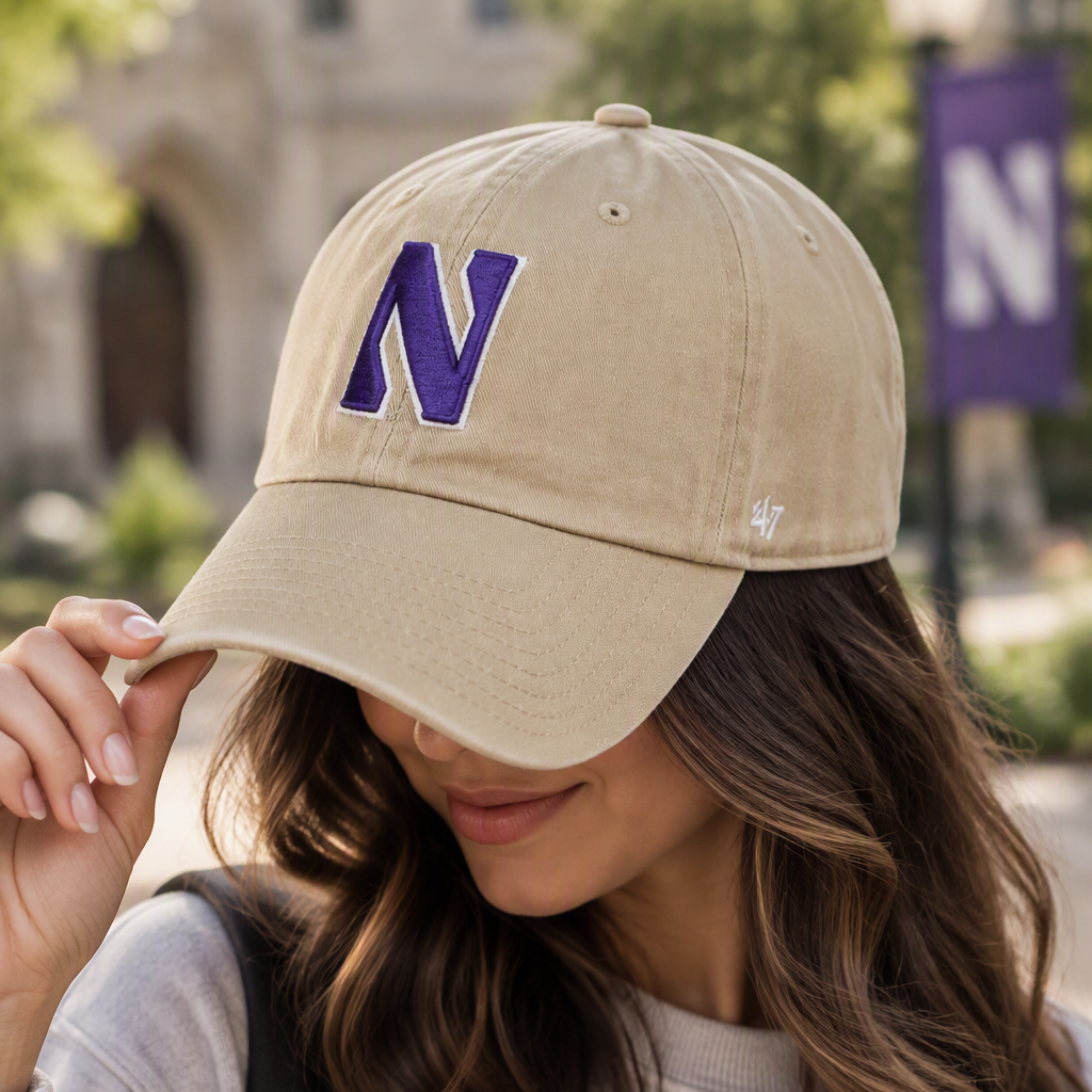 A woman wearing a beige baseball cap with a purple 'N' logo on the front, paired with a gray Northwestern sweatshirt, in an outdoor setting.